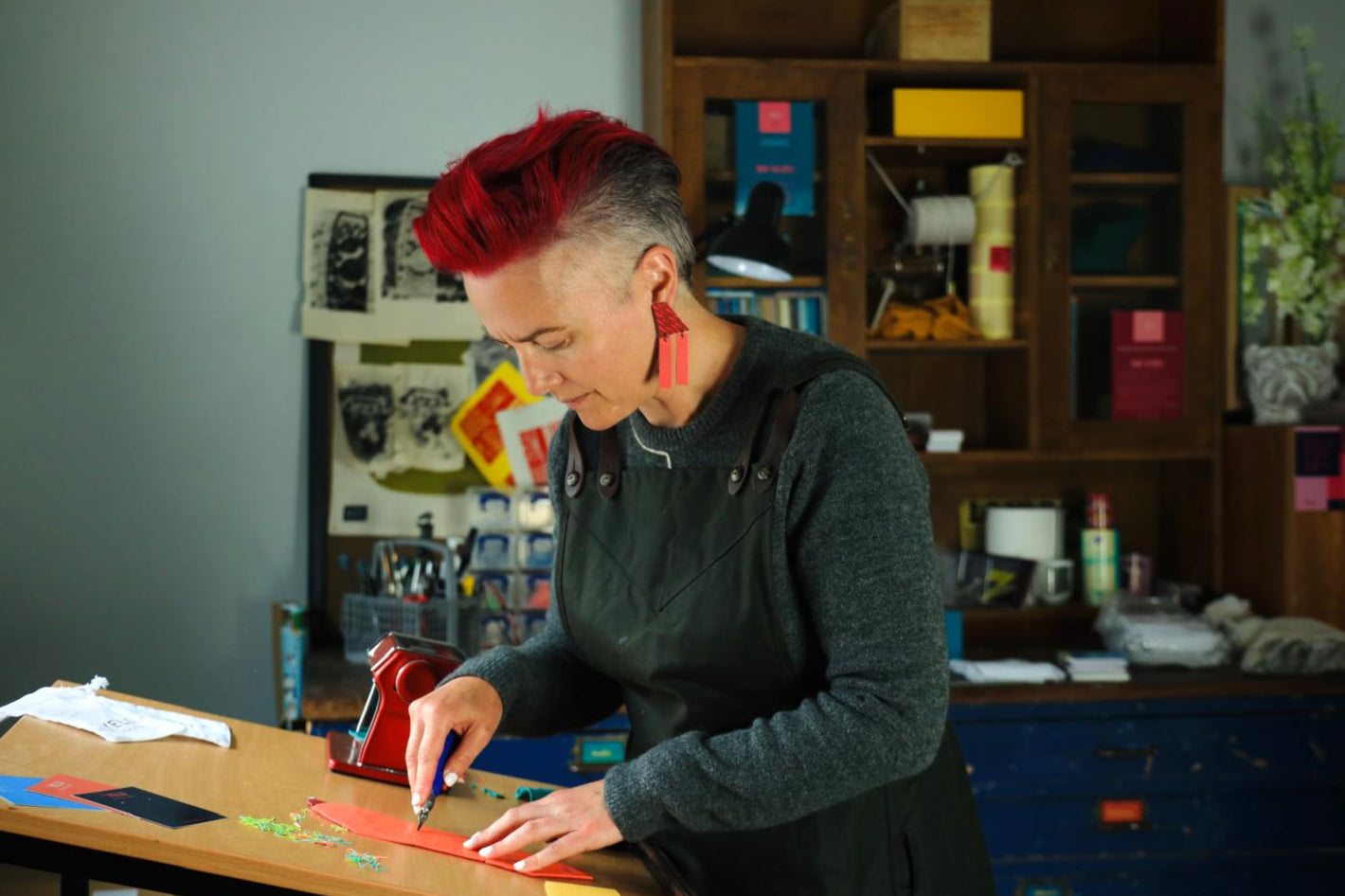 Maker and design with pink hair carving at a table in an artists studio.
